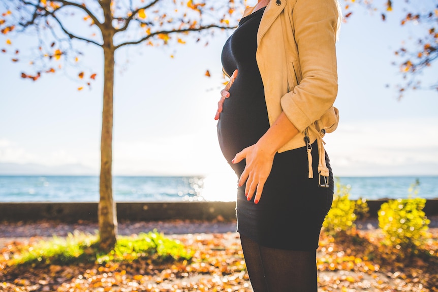 woman stands near water holding her early pregnant stomach
