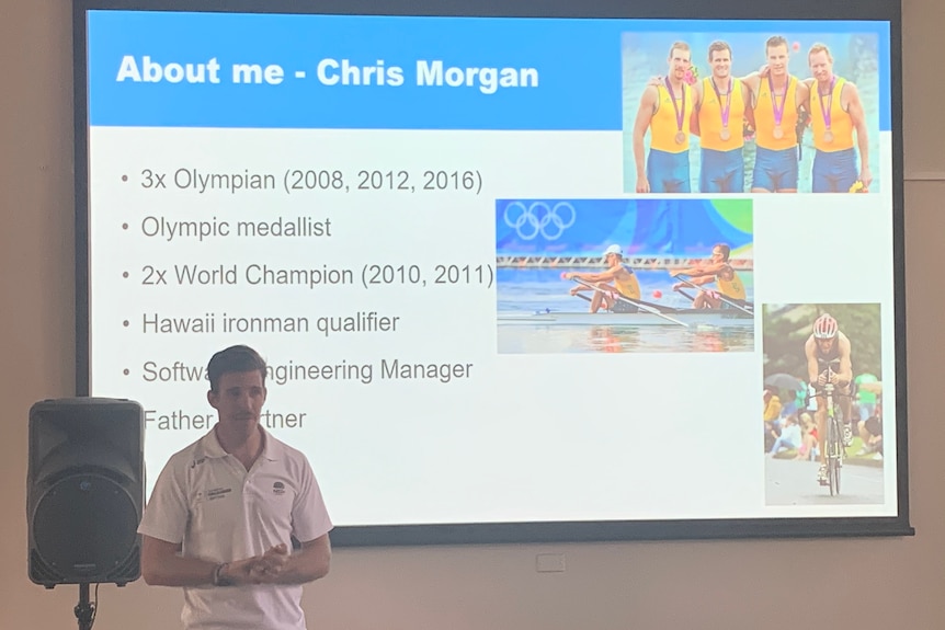 Chris Morgan stands in front of a projector and speaks.