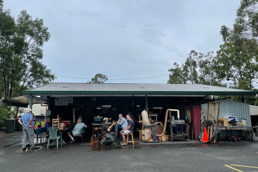 An open shed with woodworking equipment and men sitting around having morning tea.