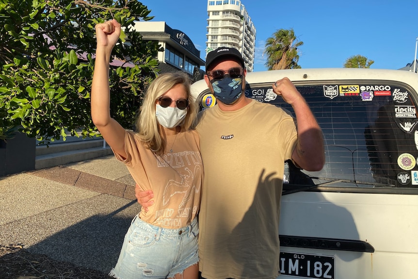 Two masked people in front of a van hold their fists aloft in triumph.