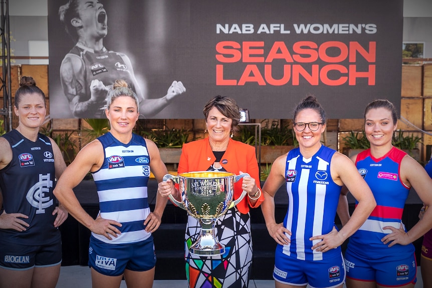 A group of female athletes poses for a group photo in front of a large sports banner