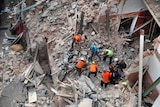 Rescuers search in the rubble of a collapsed building as seen from an aerial view.