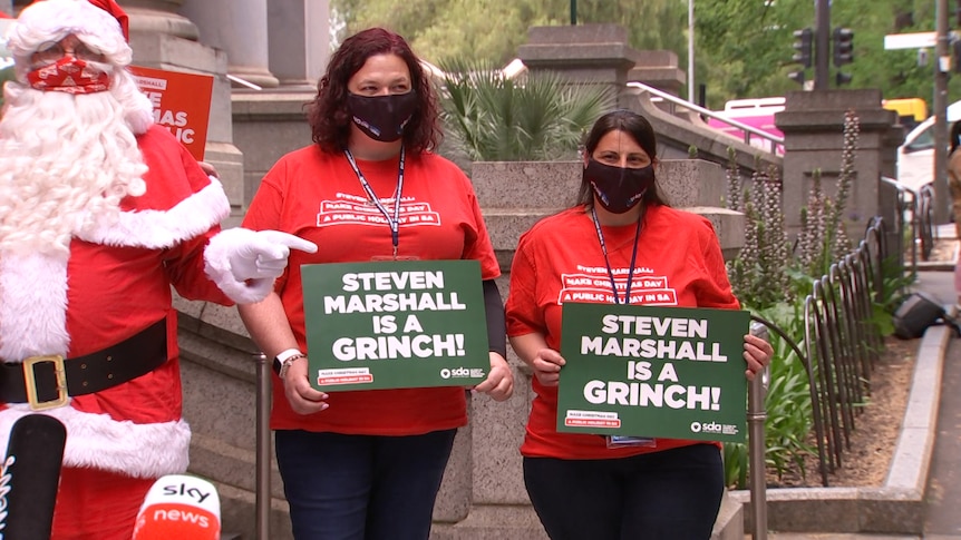 A man dressed as Father Christmas and two women holding signs 