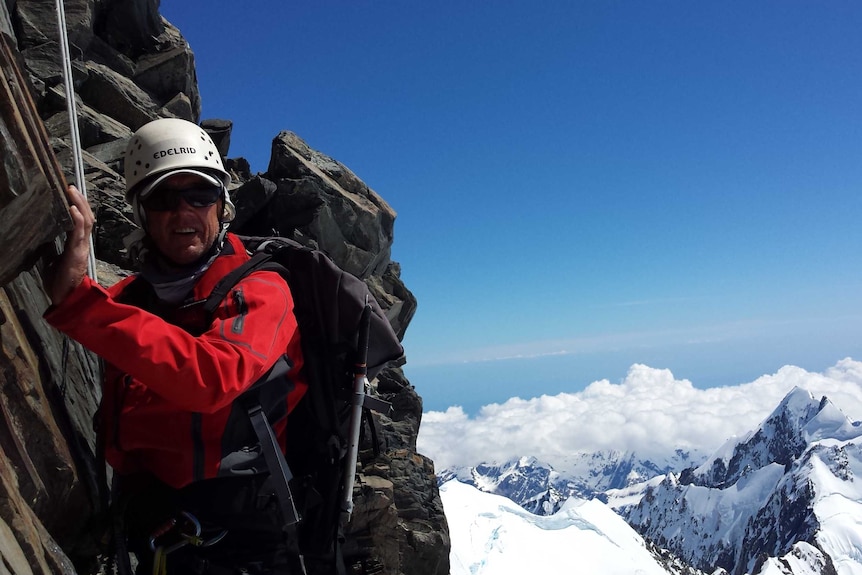 A man hiking up the side of a snowy mountain stops and smiles for a photo