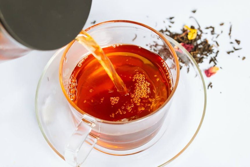 Tea is poured into a clear tea cup, as seen from above.