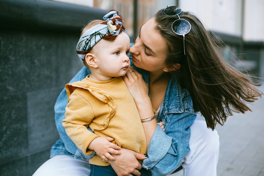 A woman with sunglasses on her head cuddles her baby from behind