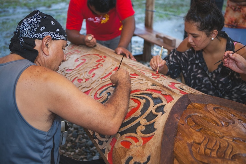 People paint red and black on a traditional carving. 