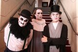 The three members of UK band The Tiger Lilies in white make-up in front of stairs.