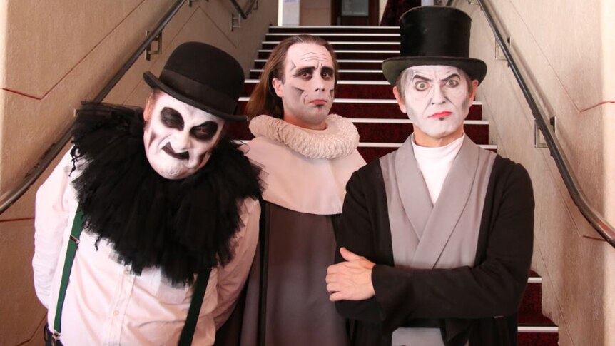 The three members of UK band The Tiger Lilies in white make-up in front of stairs.