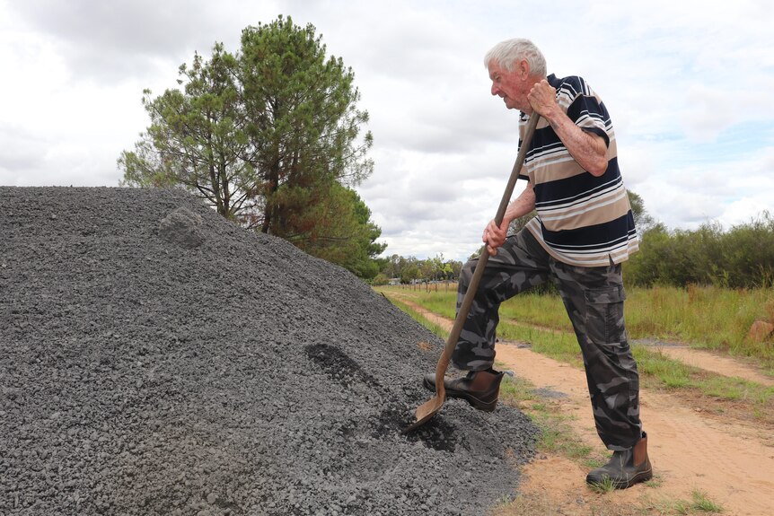 An elderly man shovels a scoop of a large pile of gravel dumped at his driveway