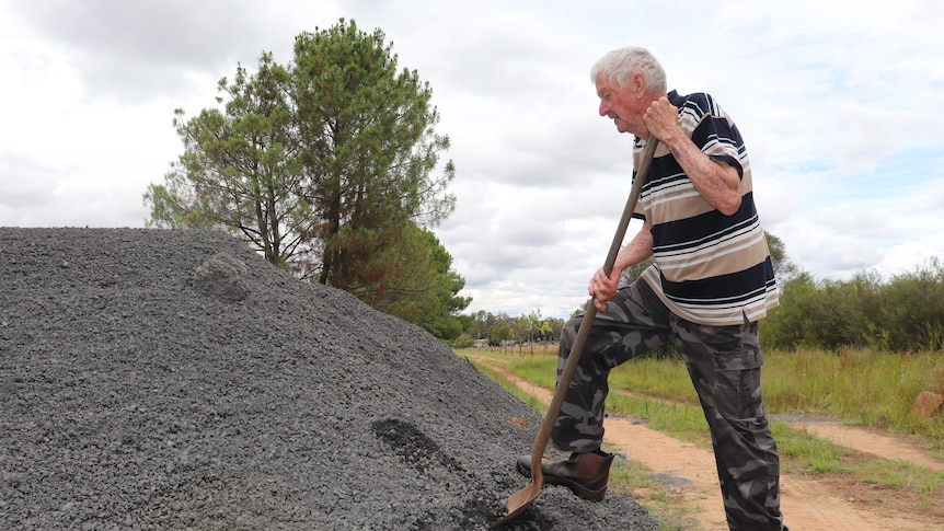 An elderly man shovels a scoop of a large pile of gravel dumped at his driveway