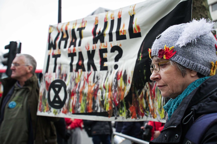 a man and a woman holding a sign that reads 'what will it take?' with the extinction rebellion logo on it