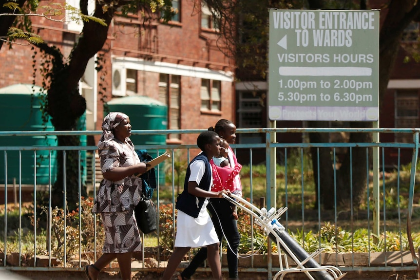 Two women and one child walk on the sidewalk outside a hospital