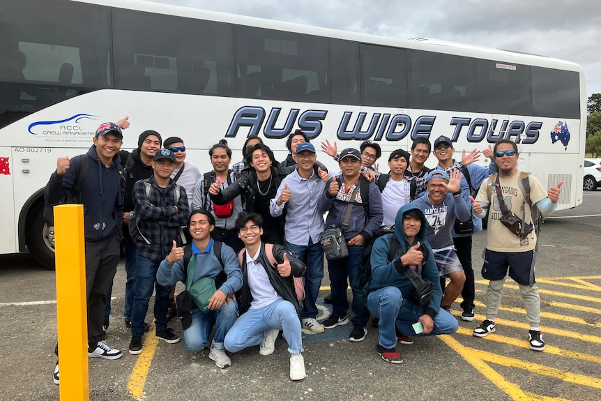 Sailors smile and give thumbs up in front of a bus