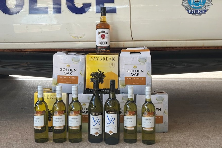 Confiscated alcohol stacked up next to a police car. 