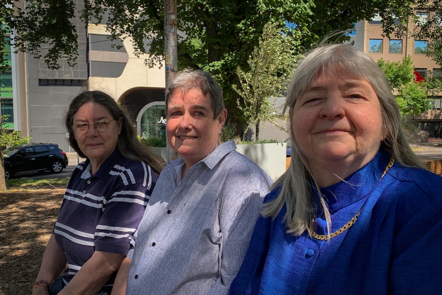 Three women sit in a row, smiling at the camera