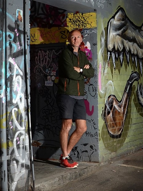 A man standing in a doorway in a graffitied alleyway.