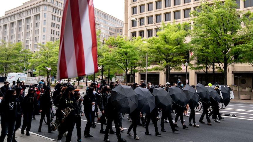 Protesters dressed in black and carrying black umbrellas marching in the street