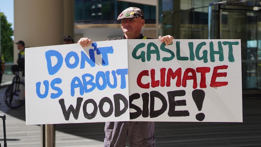 Protester with 'Don't gaslight us about climate Woodside' sign