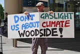 Protester with 'Don't gaslight us about climate Woodside' sign
