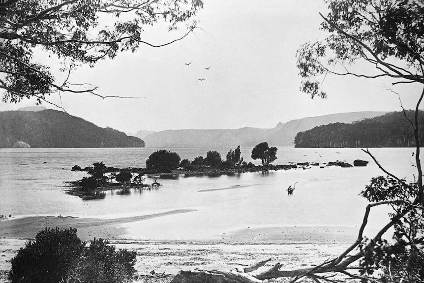 Black and white photo of a lake with a small island in the foreground and mountains in the distance