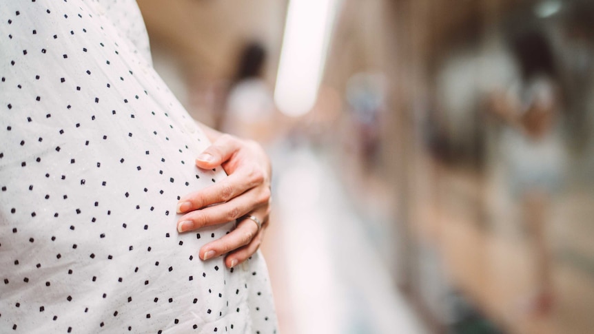 A pregnant woman touching her baby bump while waiting at a train platform.
