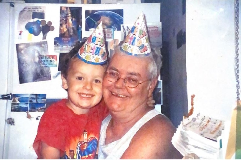 A smiling man with a little boy. Both wear party hats.