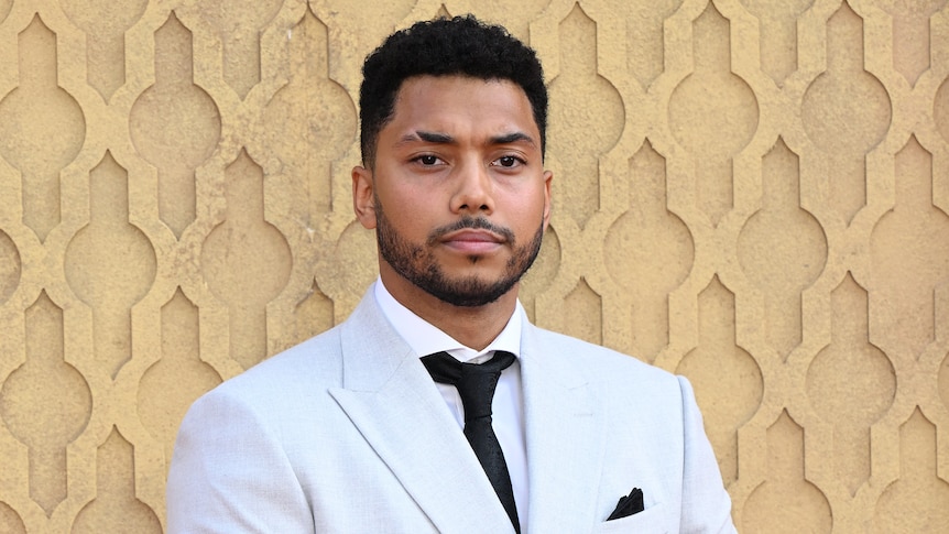 Chance Perdomo attends a premier. He's standing with a white suit on and black tie. 