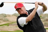 Donald Trump smiles and swings his golf club.