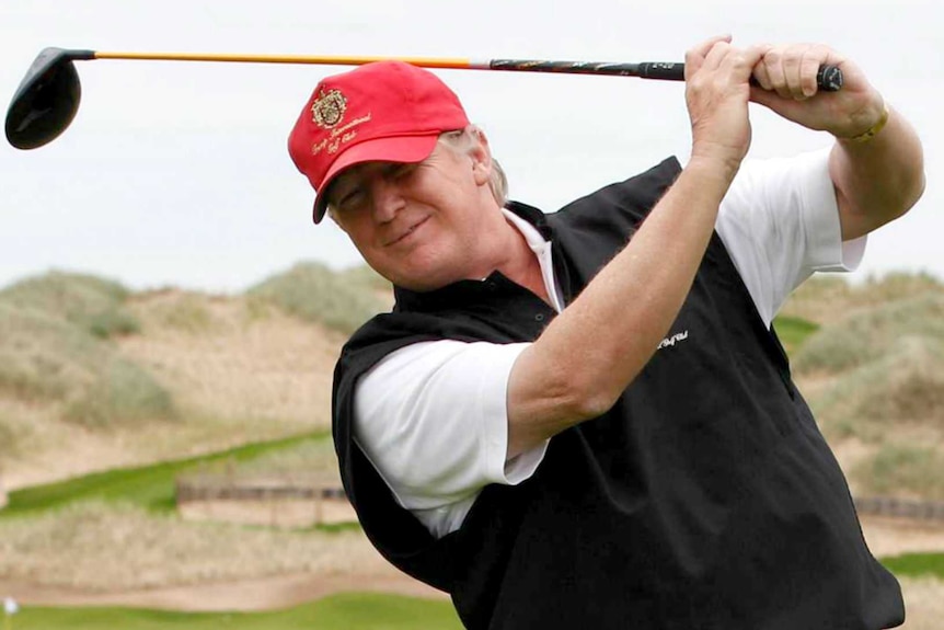 Donald Trump smiles and swings his golf club.