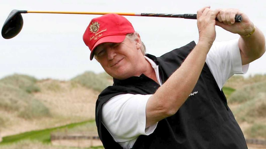 Donald Trump smiles and swings his golf club.