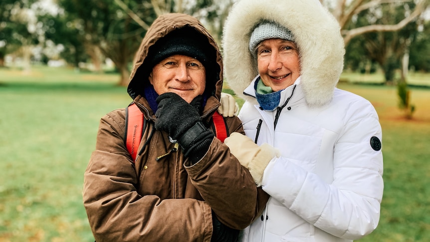 a man and woman in a park wearing hooded jumpers and glvoes