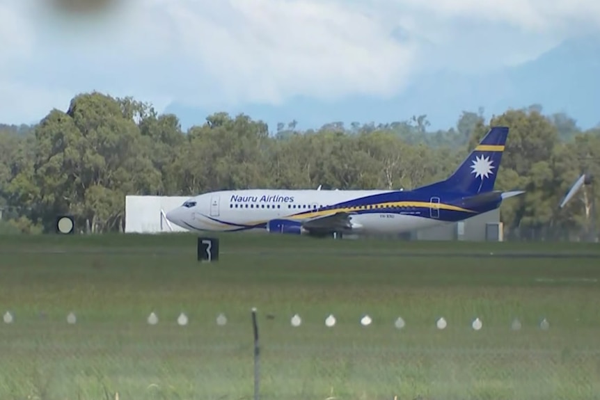 A Nauru airlines plane is seen on a runway with grass in the foreground.