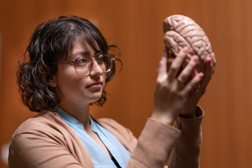 A woman holds a model of a brain up to the light.