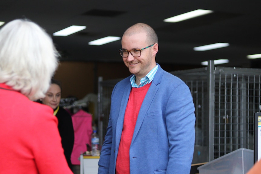 A smiling man talks to some women at a clothing collection centre. 