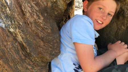 Boy sitting in a hollow of a cliff with a blue tee shirt on.