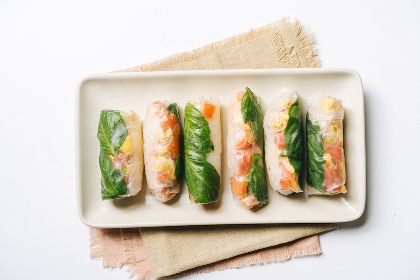 A rectangular plate with six freshly made rice paper rolls, filled with basil, vermicelli, tomato and egg.