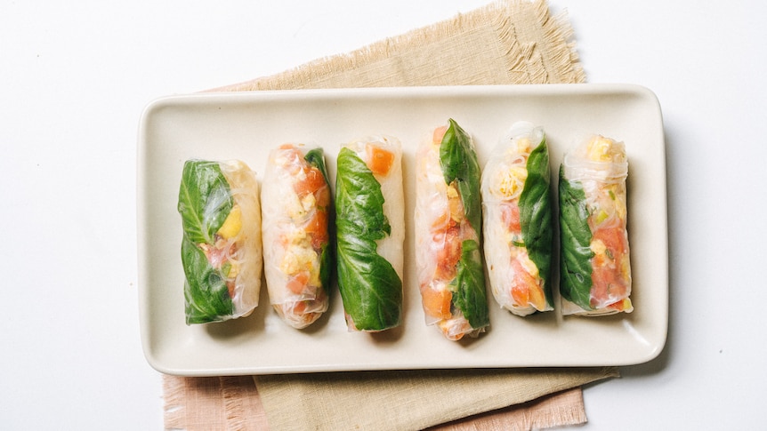 A rectangular plate with six freshly made rice paper rolls, filled with basil, vermicelli, tomato and egg.