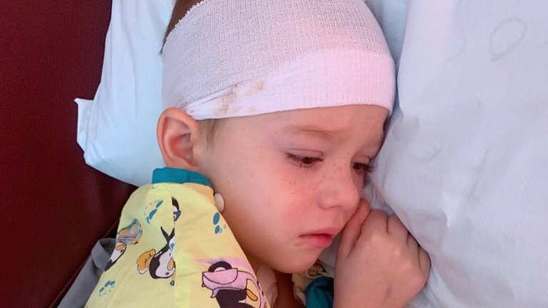 Young boy looking sad on a hospital bed with a bandage around his head
