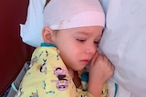 Young boy looking sad on a hospital bed with a bandage around his head