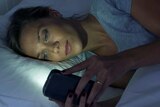 Woman lying on her side in bed using mobile phone with light from screen reflected on her face