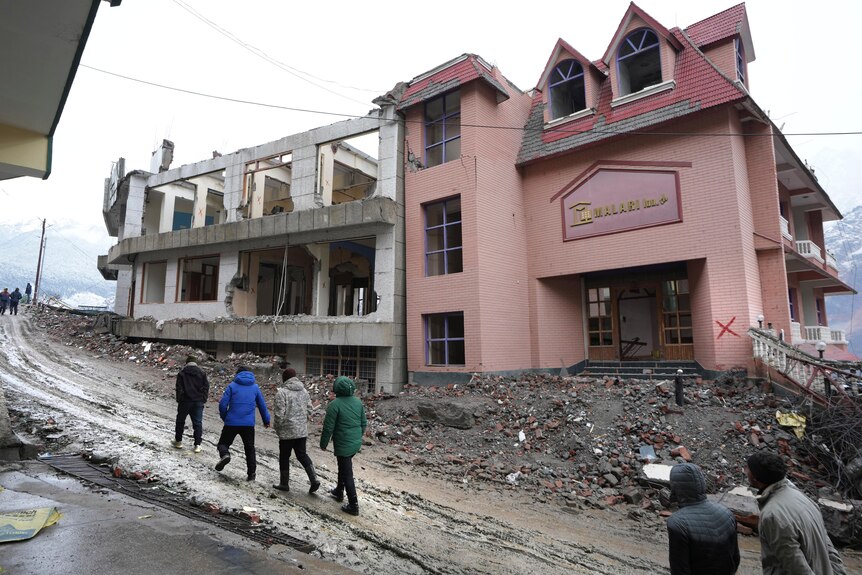 People walk by a large hotel that is being demolished.