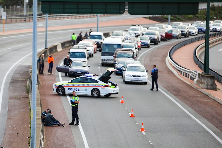 A man sitting on a freeway with police officers next to him.