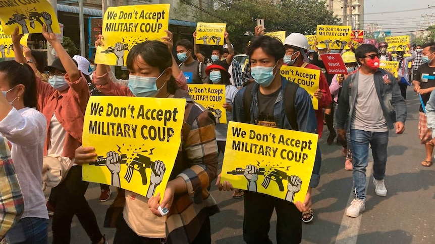 Protesters hold yellow signs that read 'we don't accept military coup'.