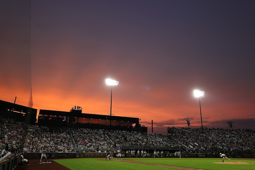 A baseball field with the sun setting behind the stands