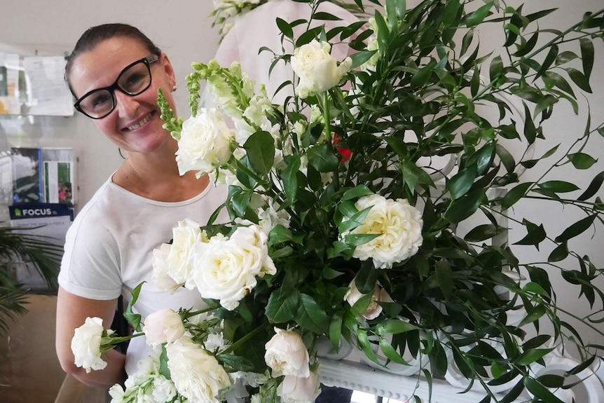 Florist Angie Kowal smiles as she holds a floral arrangement for a wedding in Brisbane.