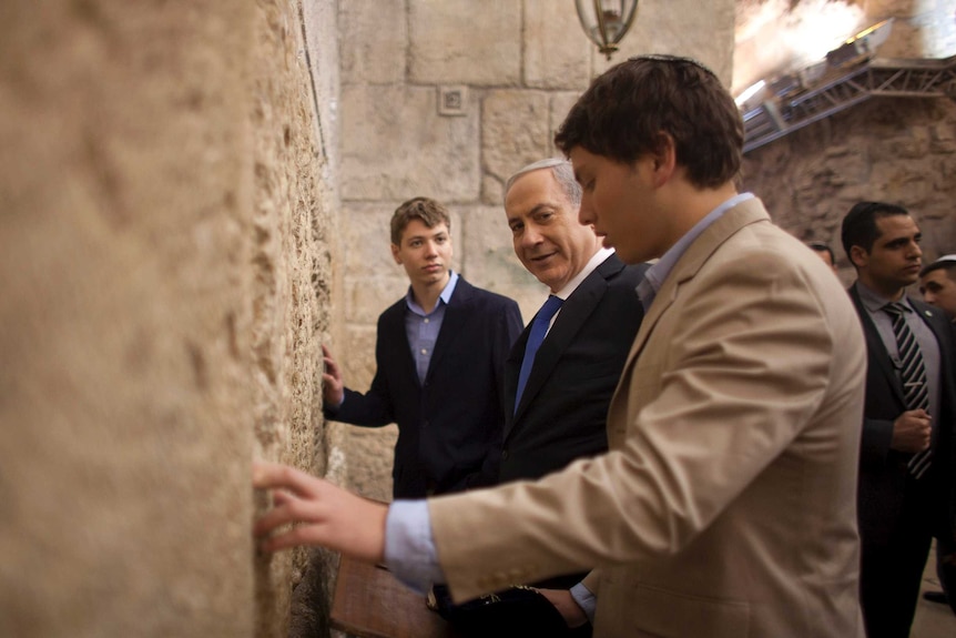 Two boys and their father pray by a wall