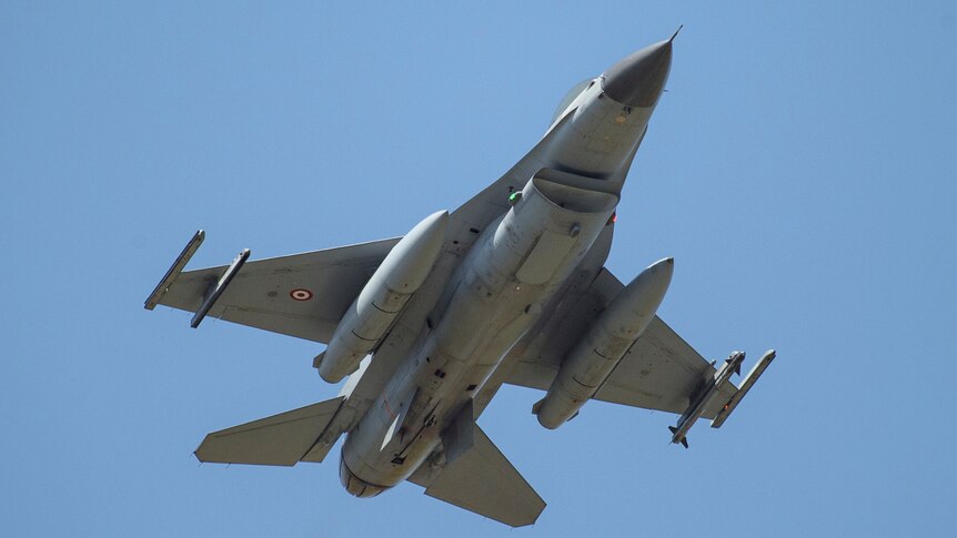 A grey F16 fighter airplane takes off into a clear blue sky.