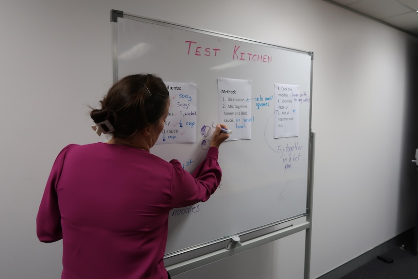 A teacher at Ipswich Community Youth Service writes cooking instructions on a whiteboard