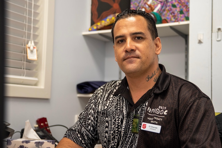 A young man in a dark shirt sits in an office.